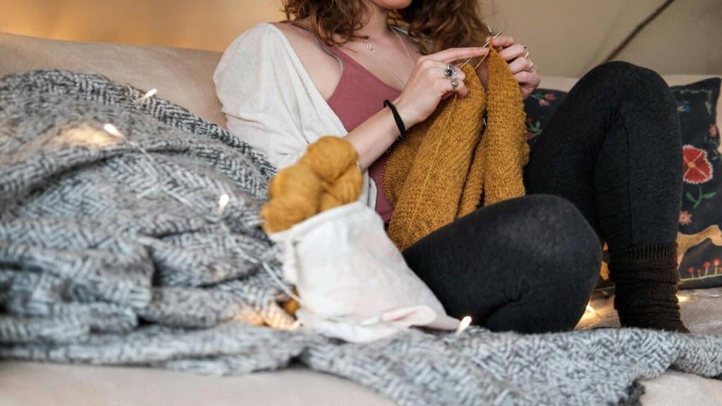 A woman knitting on the sofa.