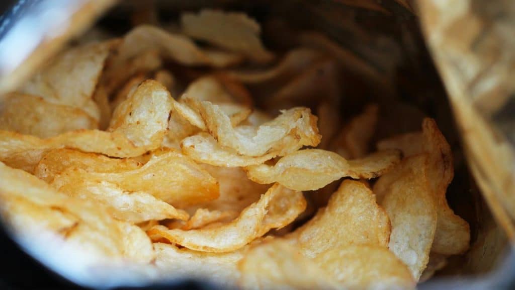 A close-up of crispy golden potato chips inside an open foil bag.