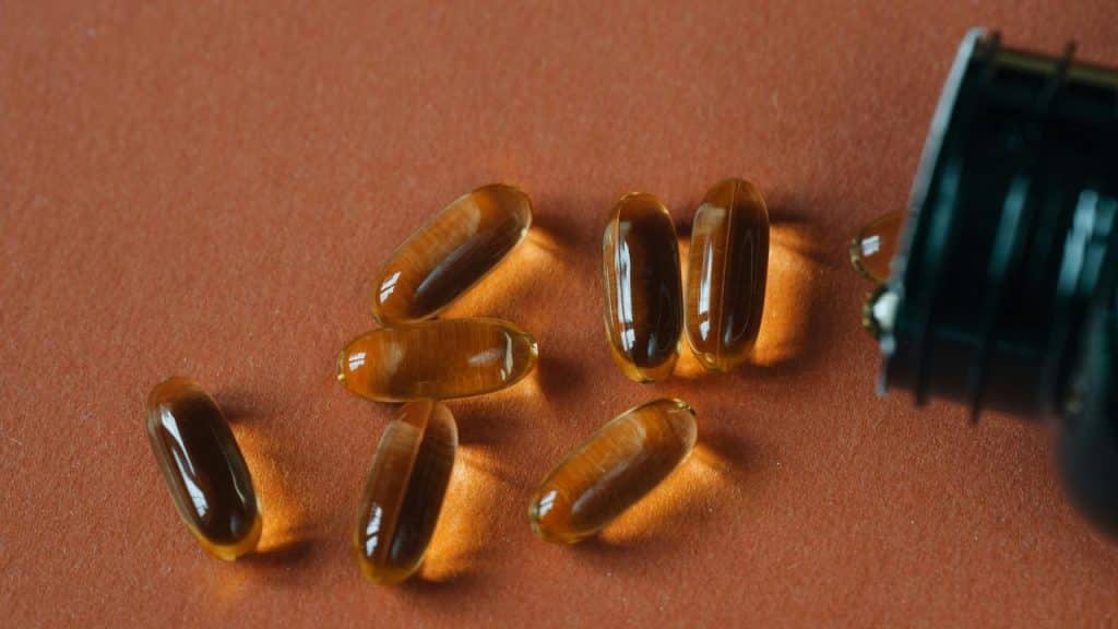 A cluster of amber softgel capsules spilling from a dark bottle onto an orange surface.