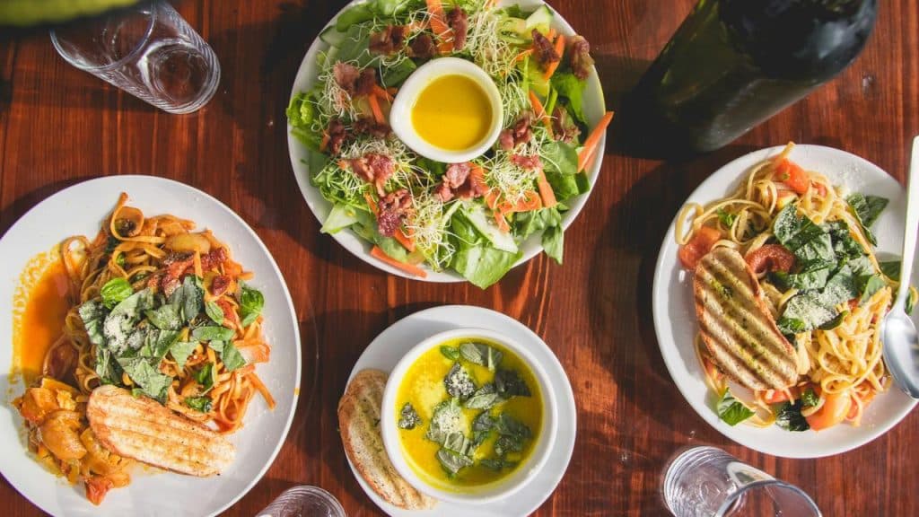 A spread of two pasta plates, a sprout salad, and basil soup with bread on a wooden table.