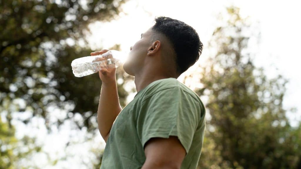 A person in a green shirt drinking water from a plastic bottle outdoors.