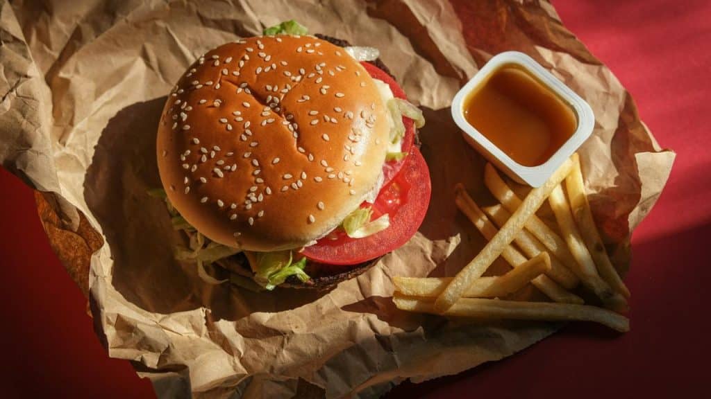A sesame-seed burger with lettuce and tomato beside fries and dipping sauce on crumpled paper.