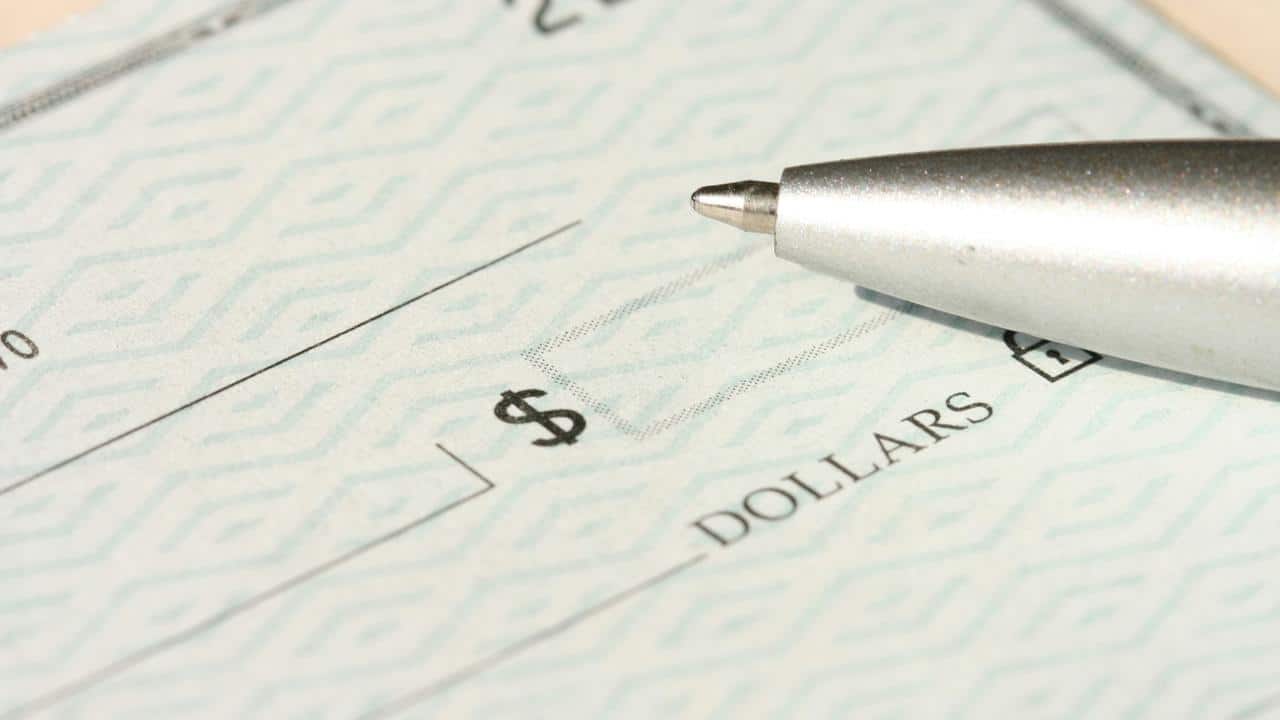 A close-up of a silver pen tip resting on a blank check next to the dollar amount box.