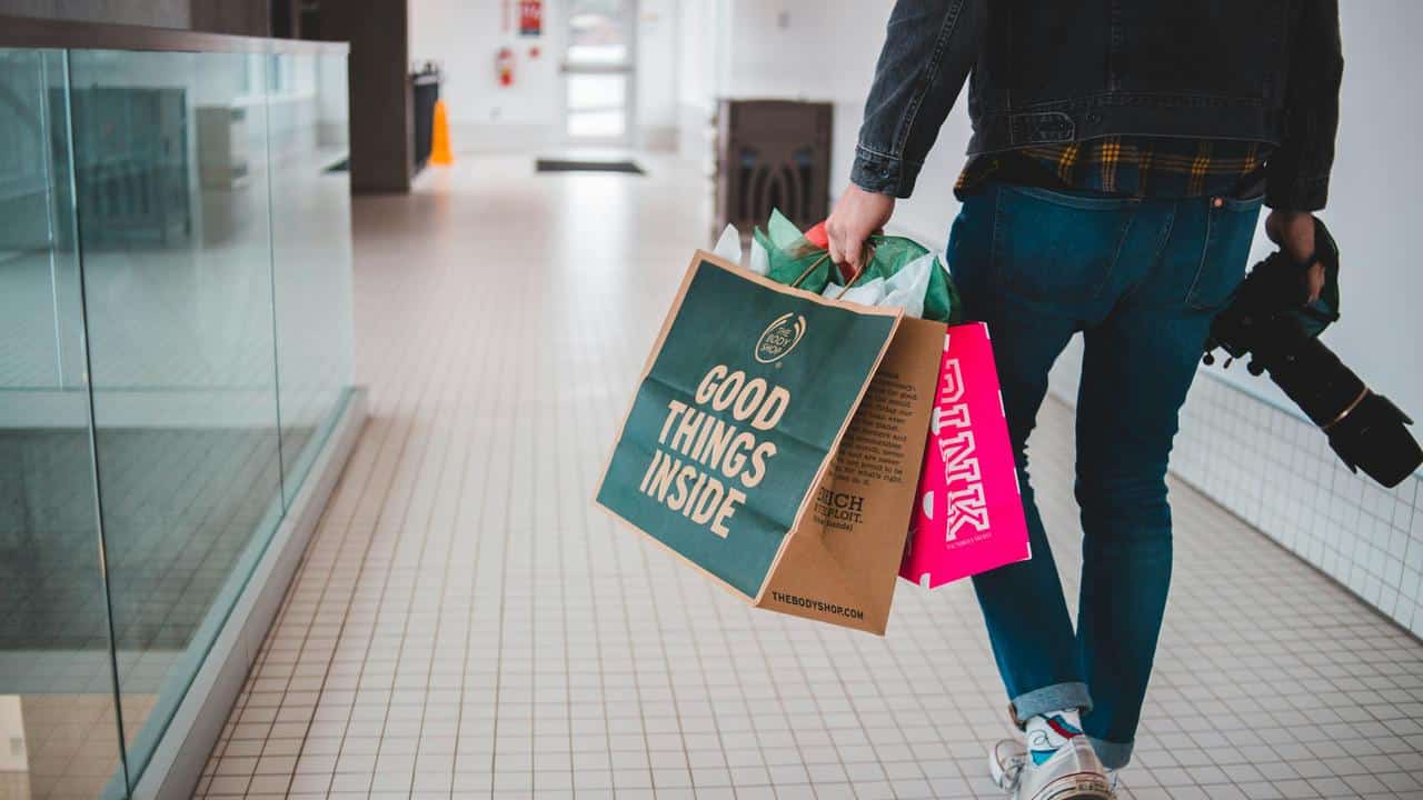 A person walking indoors holding colorful shopping bags and a camera.