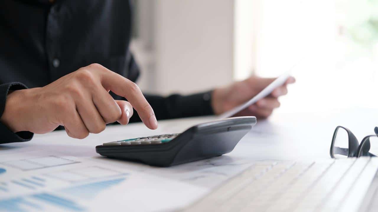 A hand holding a remote pointed at a TV displaying the Netflix logo, flanked by two potted plants.