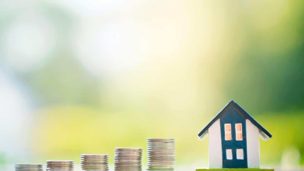 A row of ascending stacks of coins beside a miniature house model.