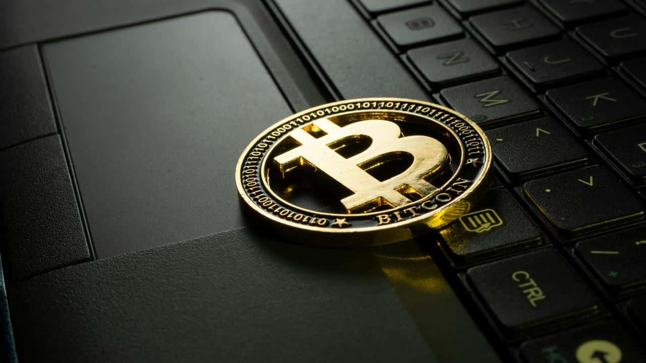 A gold Bitcoin coin resting atop a black laptop keyboard.