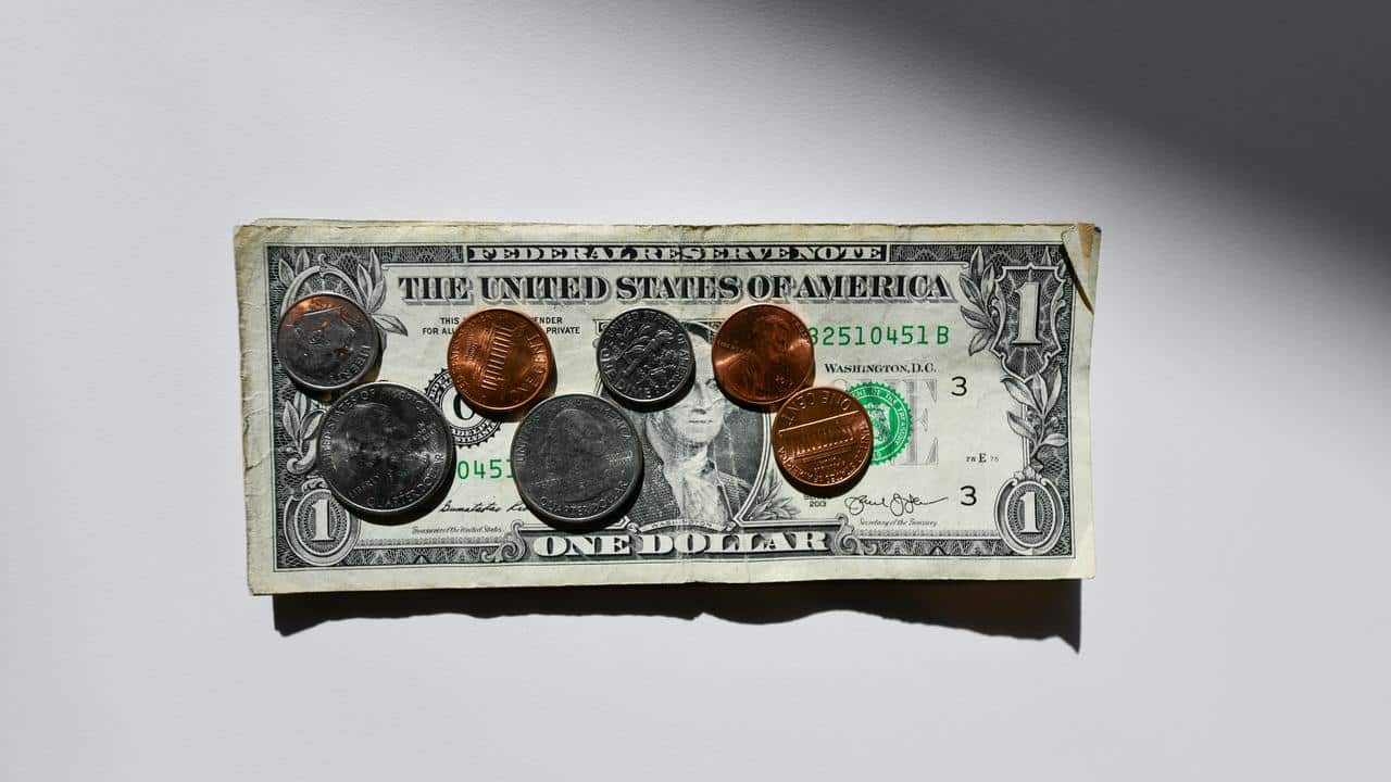A one-dollar bill topped with assorted U.S. coins on a white surface.