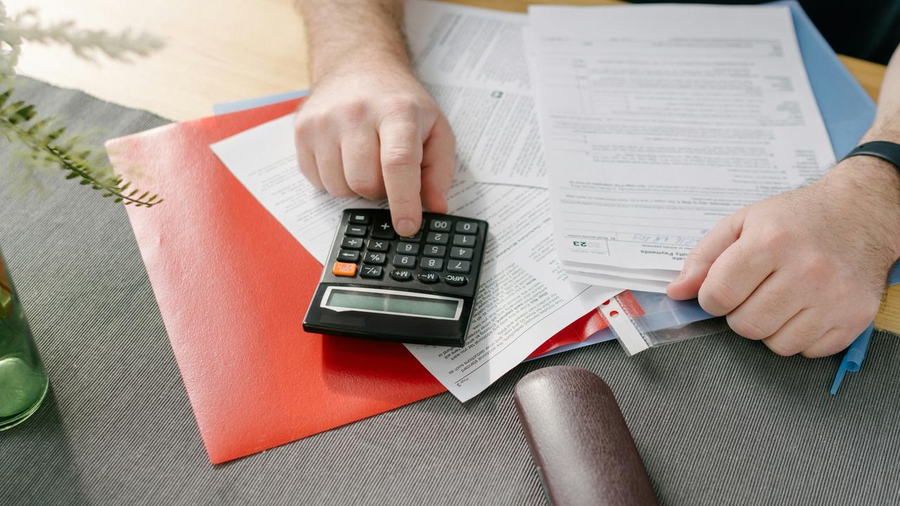 A hand pressing a calculator button atop scattered documents and tax forms.