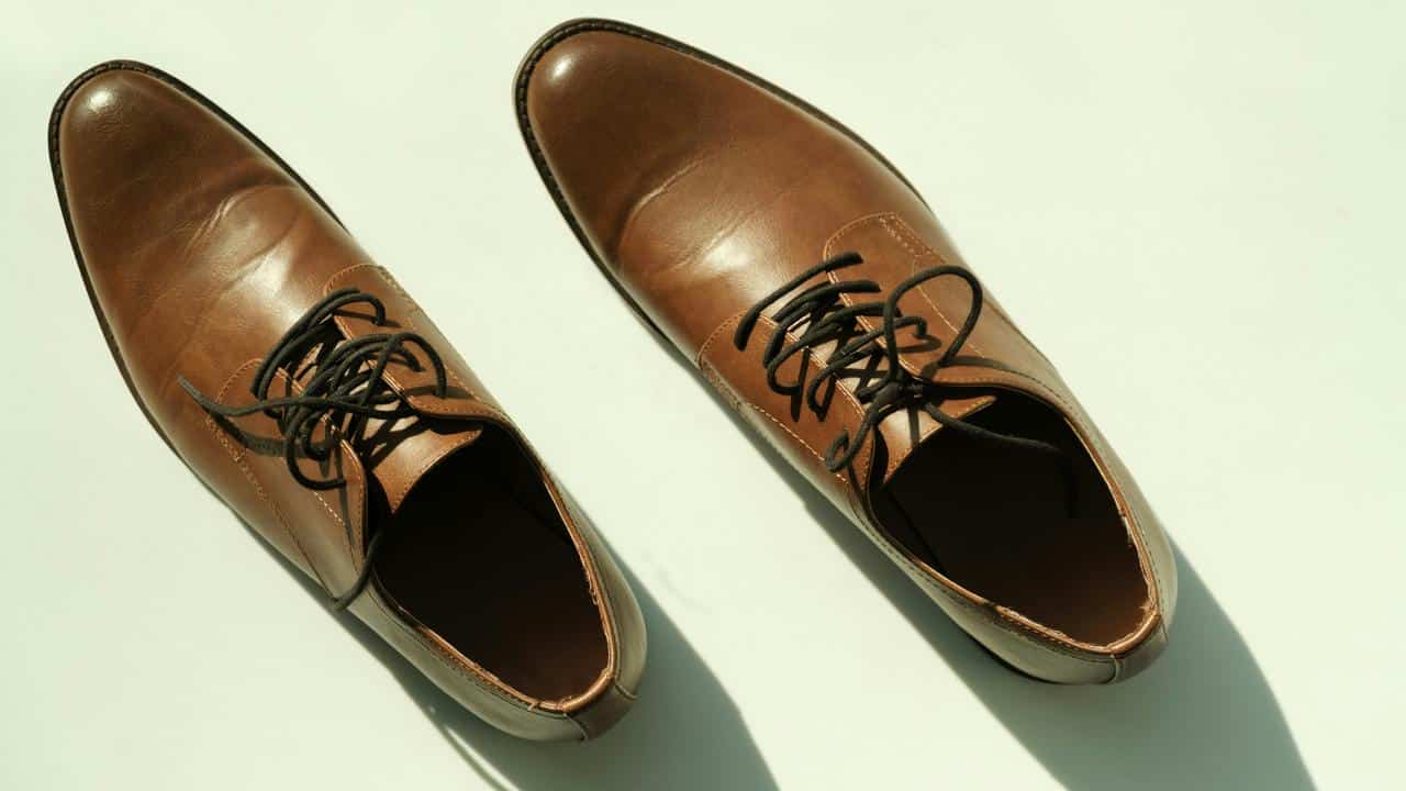 A pair of brown leather lace-up dress shoes on a white surface.