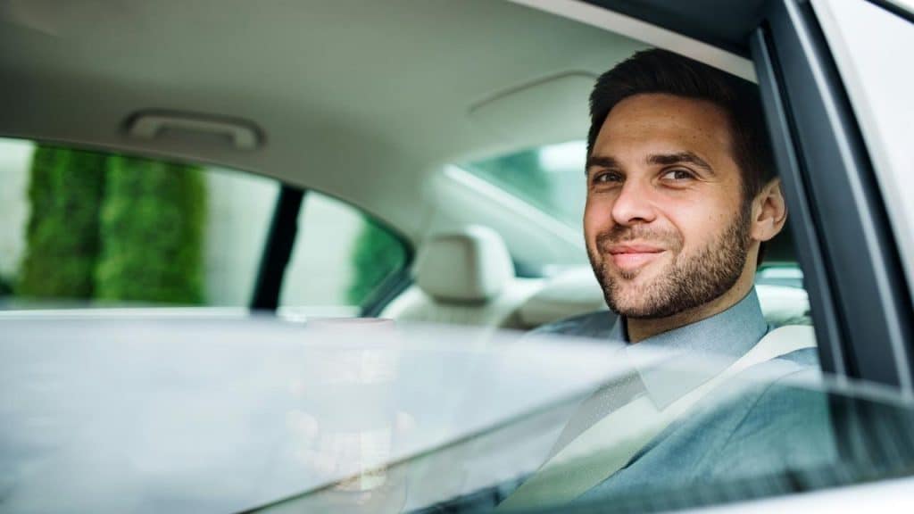 A smiling man holding a coffee cup while seated in a car.