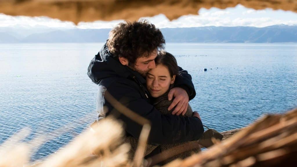 A man embracing a woman by a lakeside.