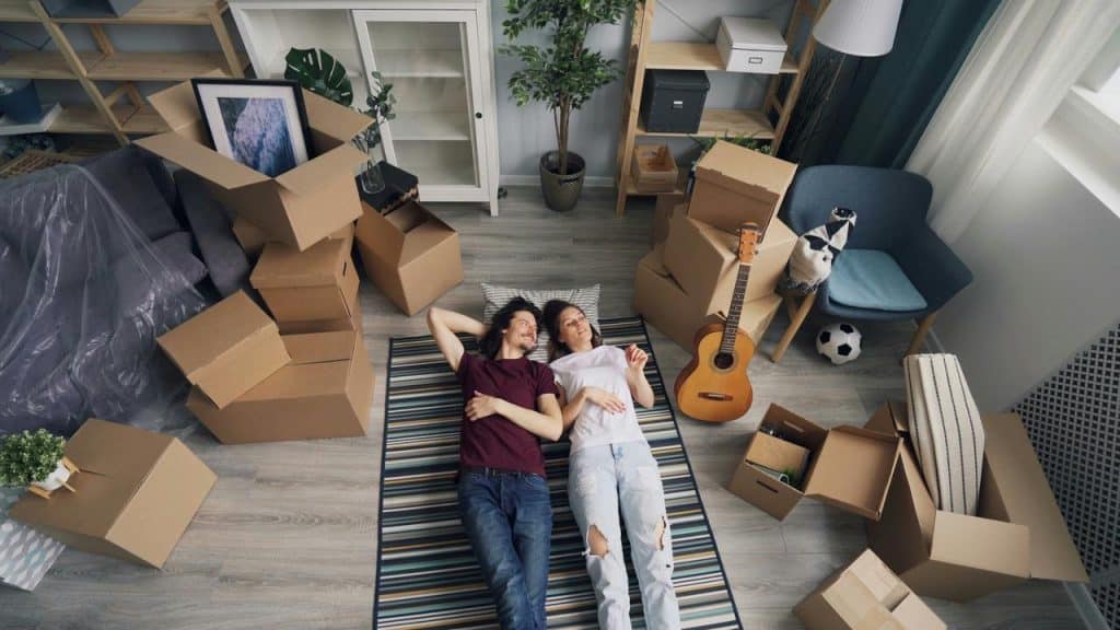 A couple lying on the floor amid packed moving boxes.