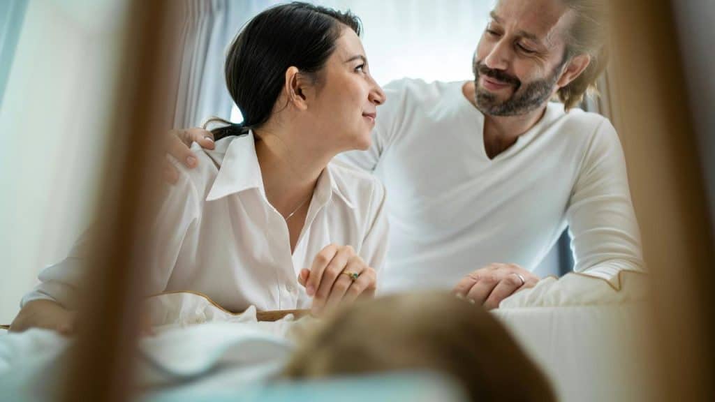 A couple leaning over a crib, gazing at each other.