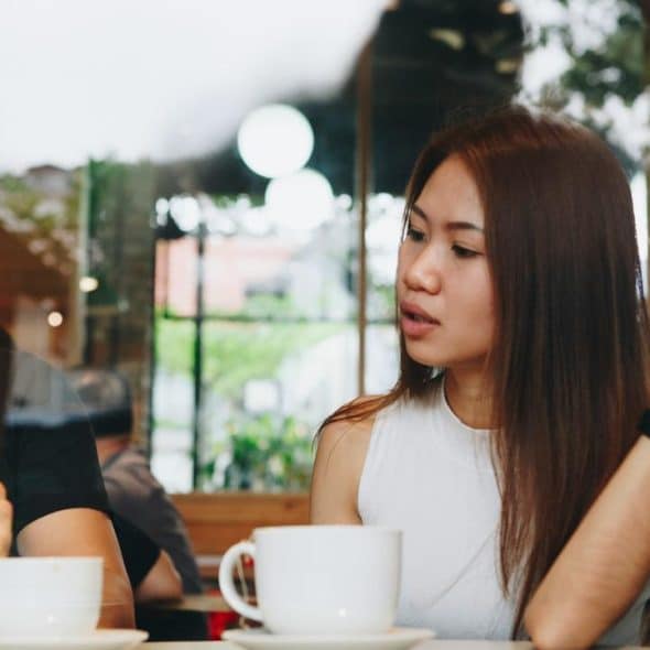 A man on his phone while a woman gestures across a café table.