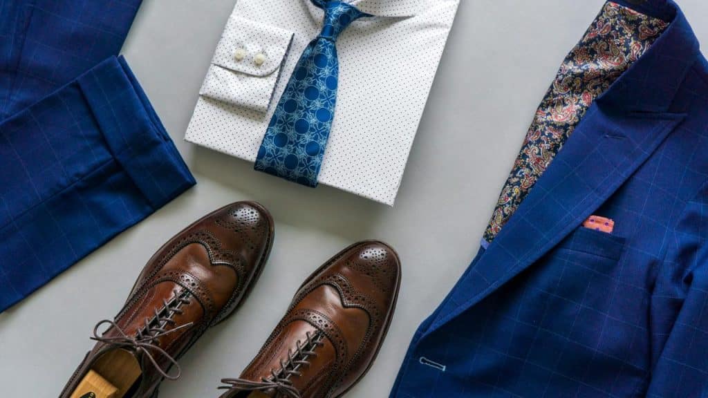 A stylish men’s outfit with a blue suit, white dotted shirt, blue tie, and brown brogue shoes.