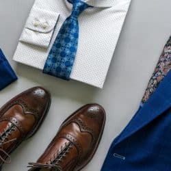 A stylish men’s outfit with a blue suit, white dotted shirt, blue tie, and brown brogue shoes.