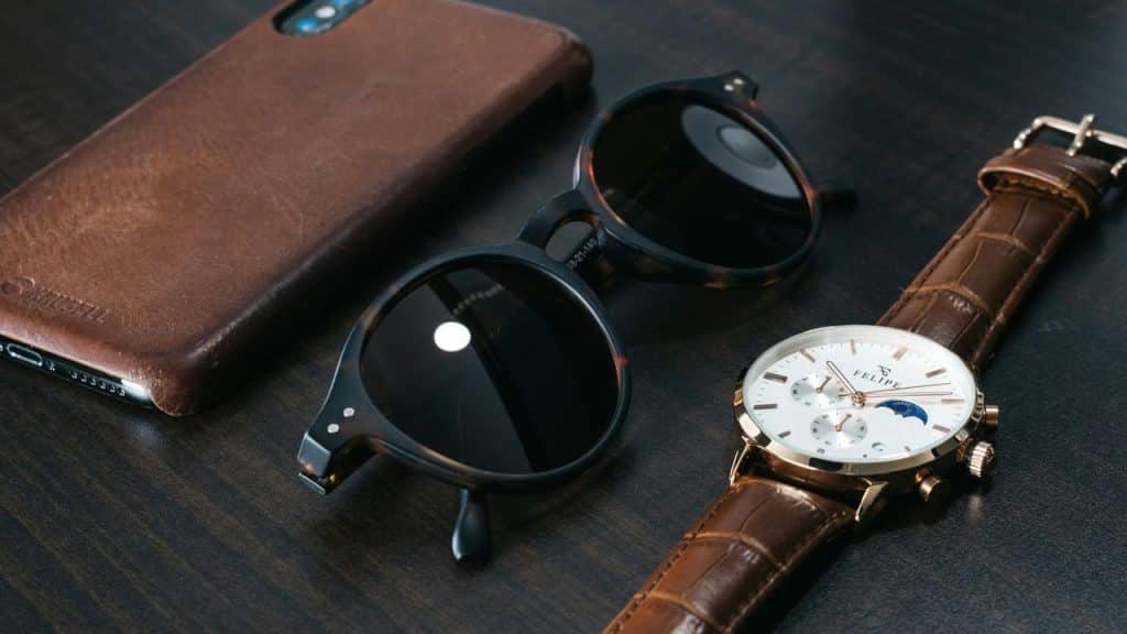 A flat lay of a leather phone case, sunglasses, and wristwatch.
