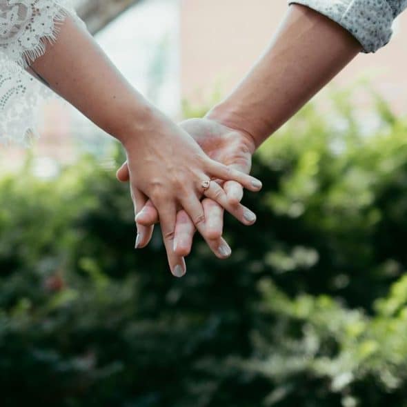 A couple holding hands, featuring a lace sleeve and engagement ring.