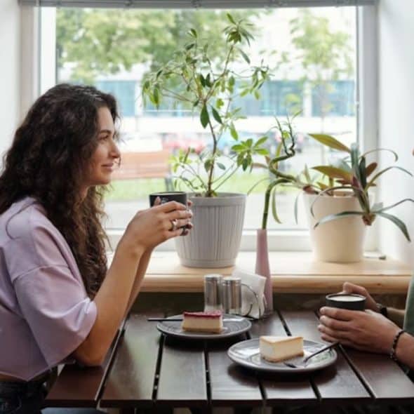 A man and woman sitting across from each other in a cozy café, talking calmly with coffee in hand