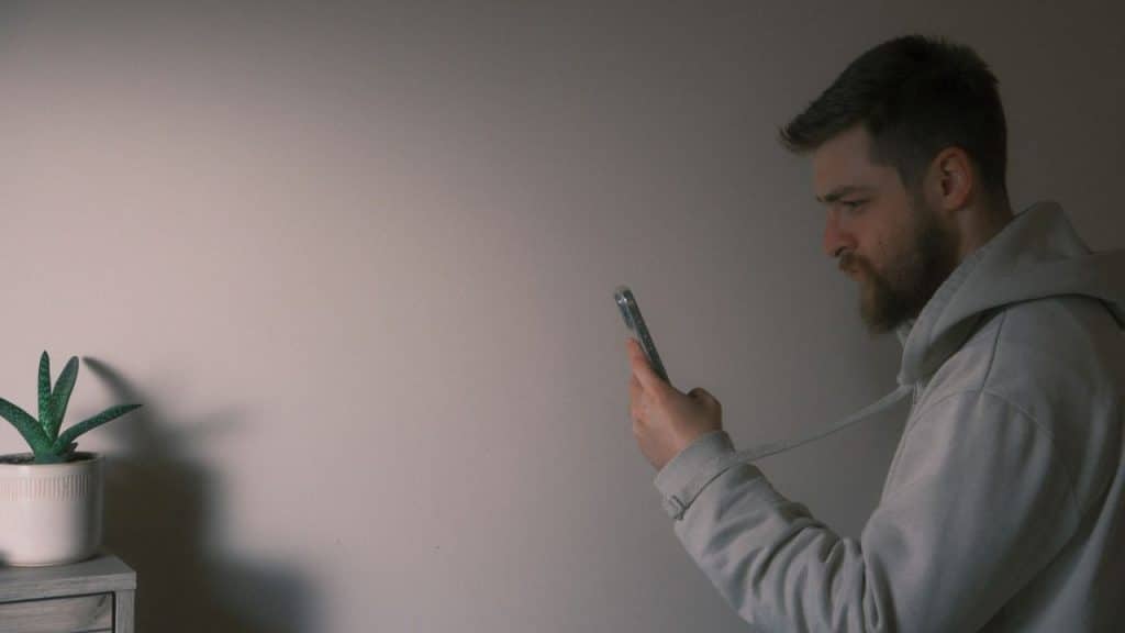 A bearded man in a hoodie looks at his phone with a serious expression.