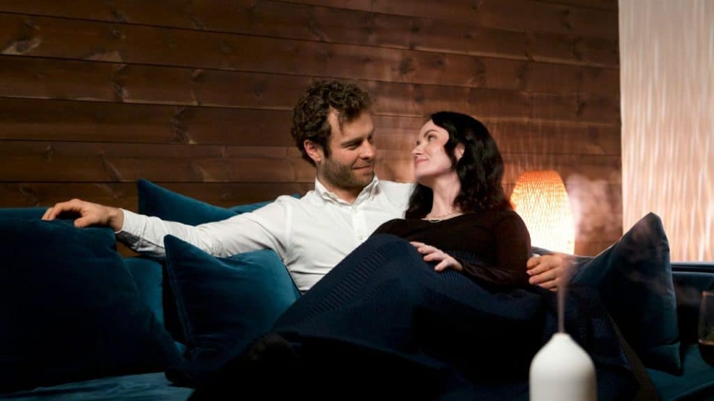 A smiling couple gazes at each other while relaxing on a blue sofa.