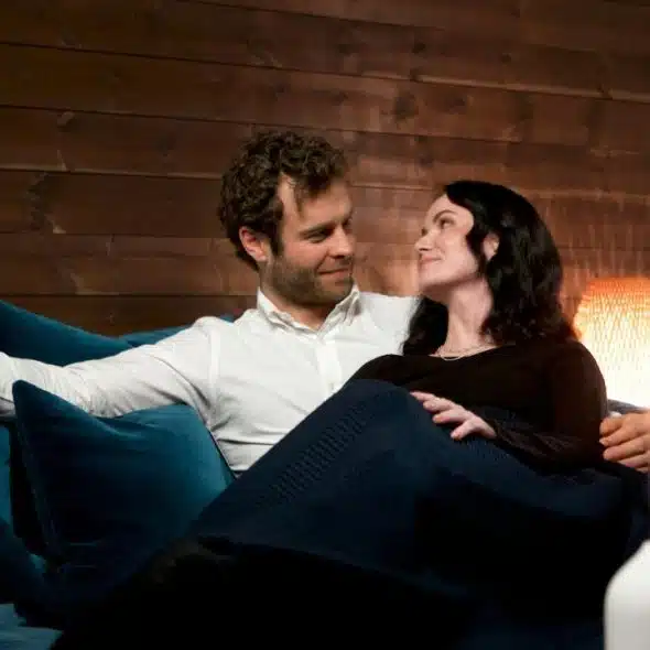 A smiling couple gazes at each other while relaxing on a blue sofa.