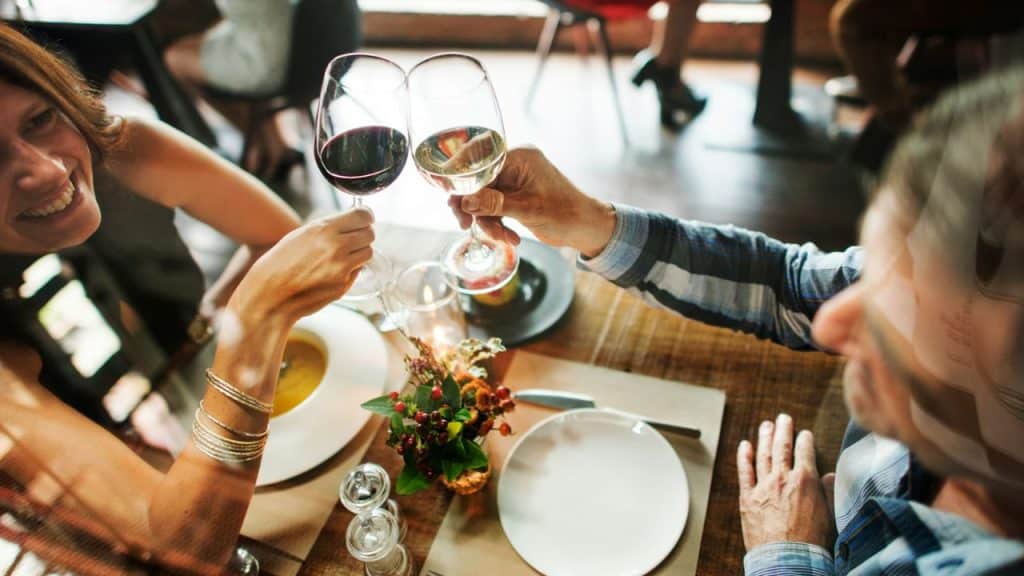 A smiling woman and a man clink wine glasses over a table with food.