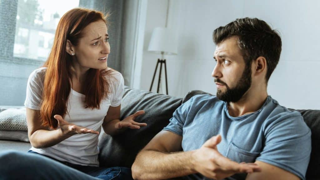 A red-haired woman with a frustrated expression gestures at a man who listens intently.