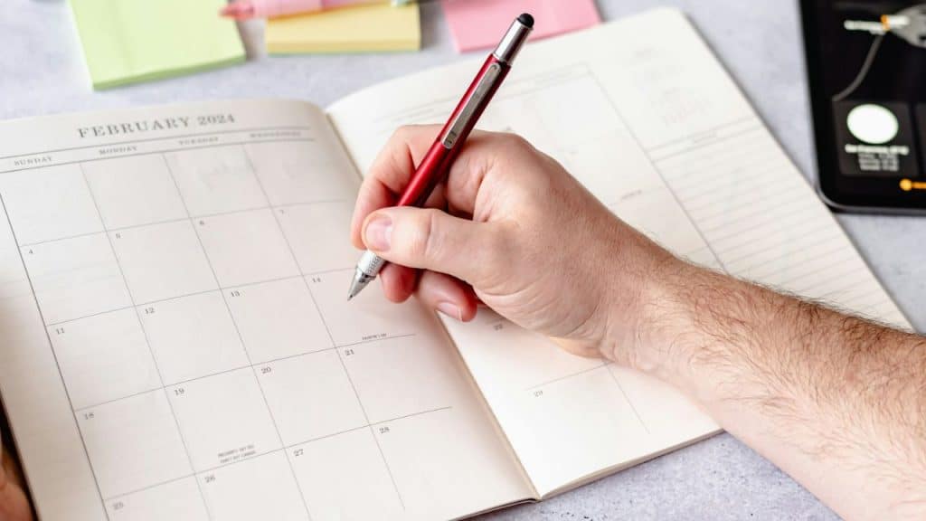 A hand with a red pen writes in a February 2024 calendar planner.