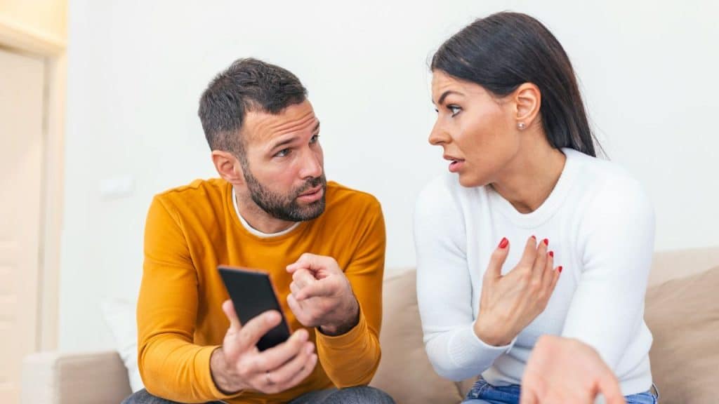 A man holds a phone while a woman gestures, both appearing to be in a discussion.