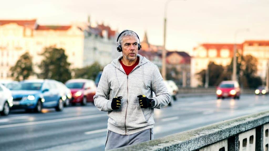 A man with headphones jogs on a city bridge with cars passing by.