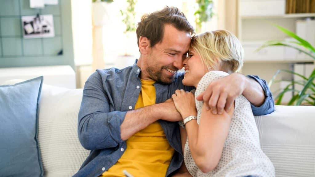 A happy couple embraces on a couch, touching foreheads and smiling.