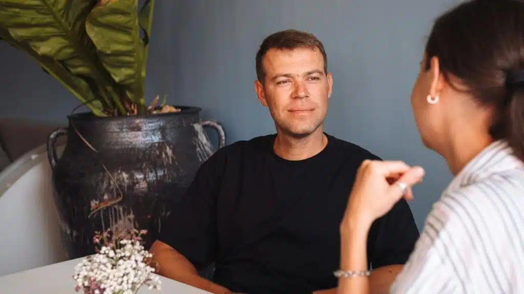 A man in a black shirt looks intently at a woman across a table.