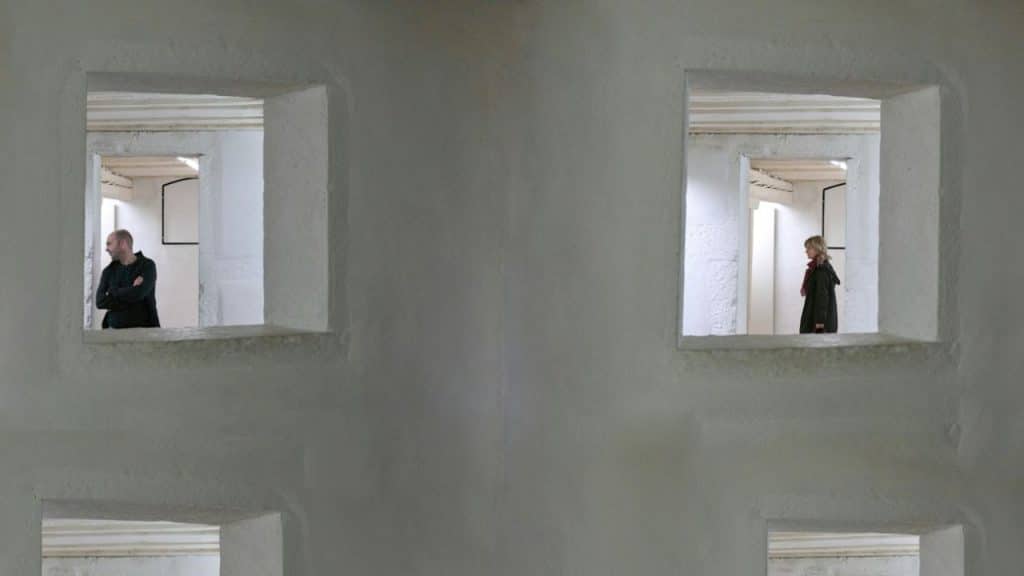 A split image shows a man and woman separately looking out of a window.