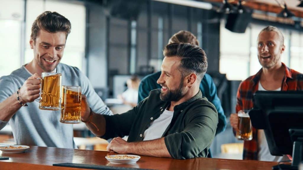 Four men are happily toasting with beer mugs at a bar.