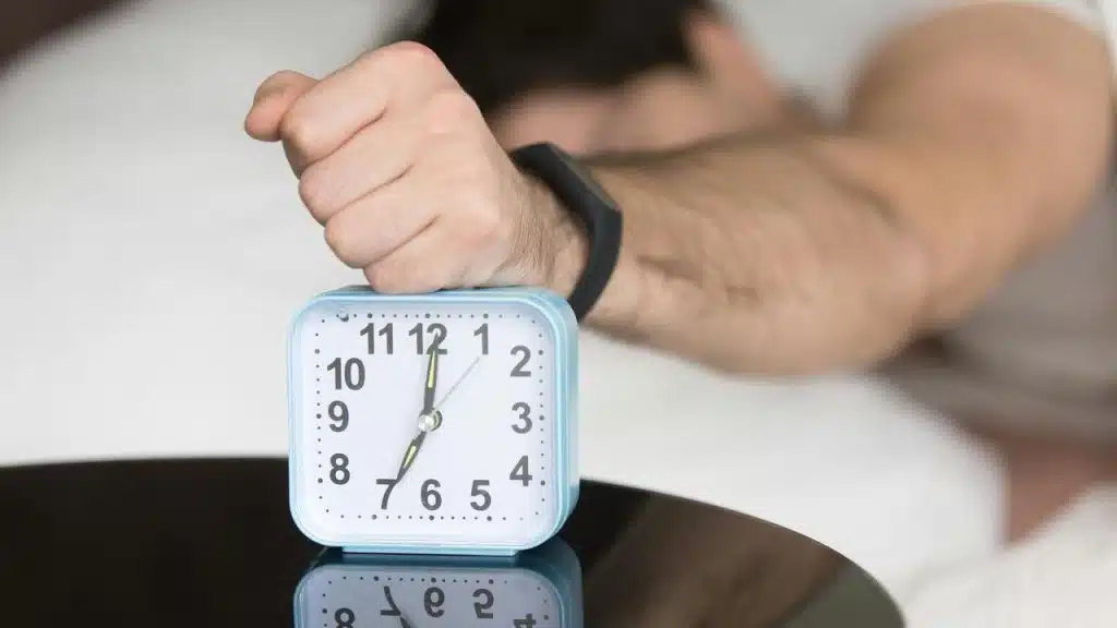 A man’s fist hitting an alarm clock on a bedside table.