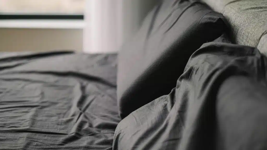 A rumpled dark sheet and pillow on a bed.