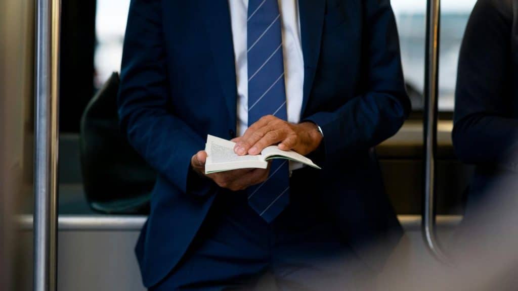 A suited man reading a small book on public transit.