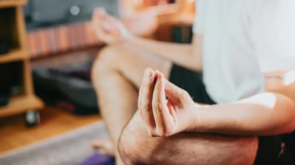 A person seated cross-legged meditating with fingers held in a mudra gesture.