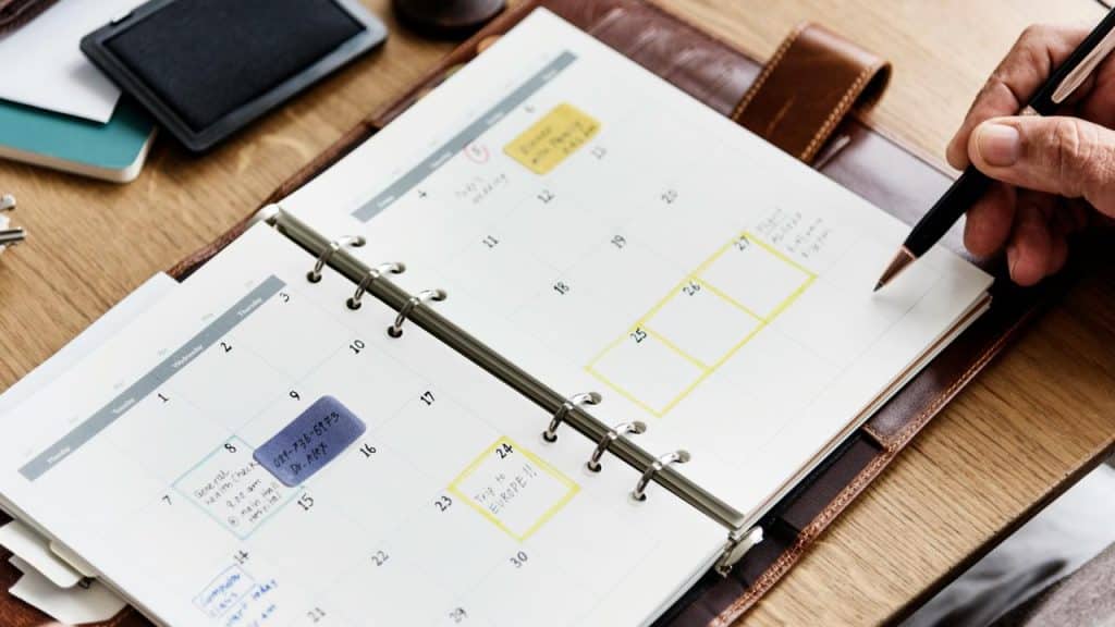 A ring-bound monthly planner open to a calendar with highlighted dates and handwritten notes.