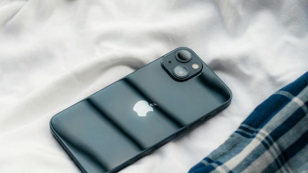 A black iPhone lying on white bedding sheets.
