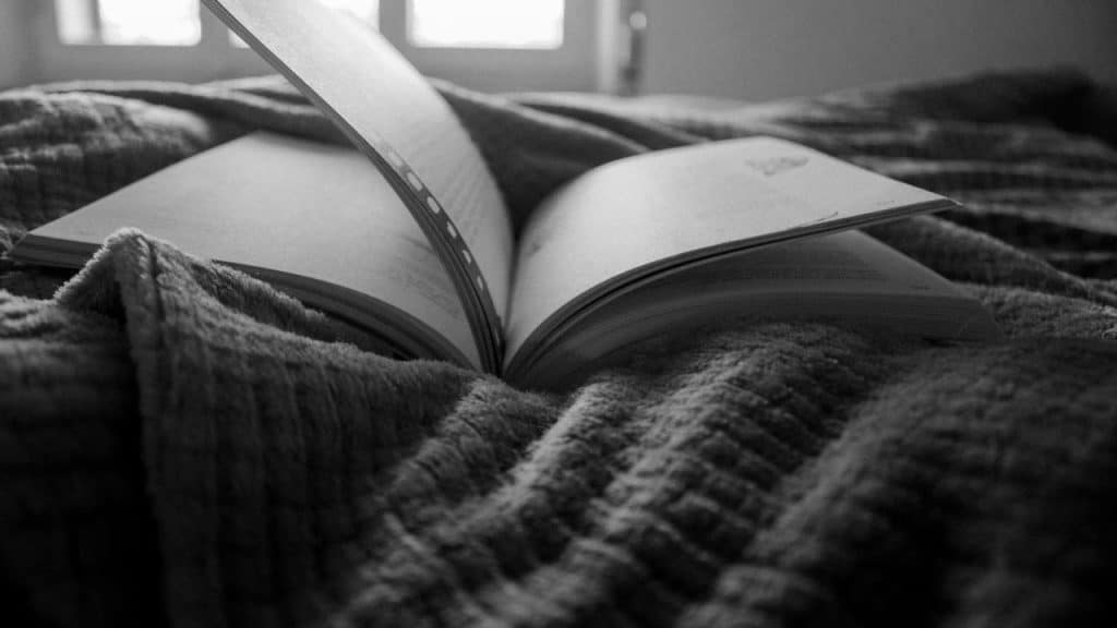 An open book with a turning page resting on a textured blanket.