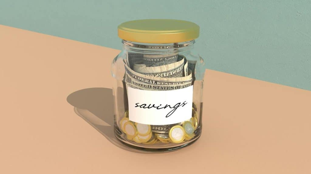 A glass jar labeled “savings” filled with rolled dollar bills and coins.