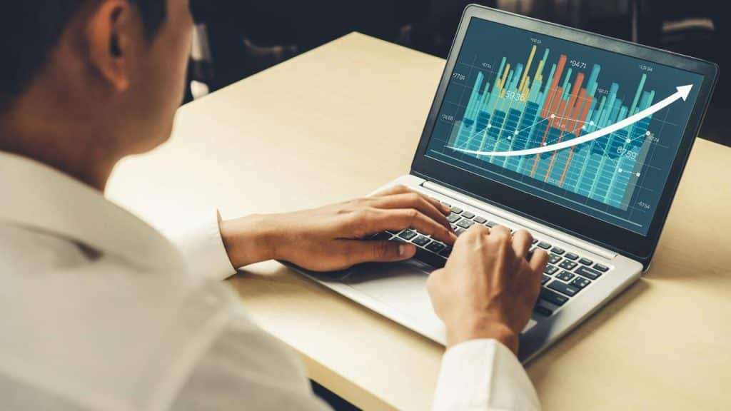 A person typing on a laptop displaying an upward-trending bar chart.