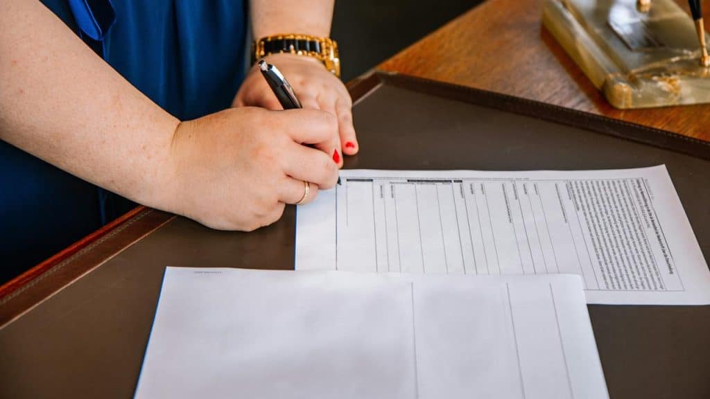 A person signing paperwork on a desk.