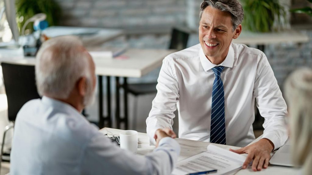 A financial advisor shaking hands with a client across a desk.