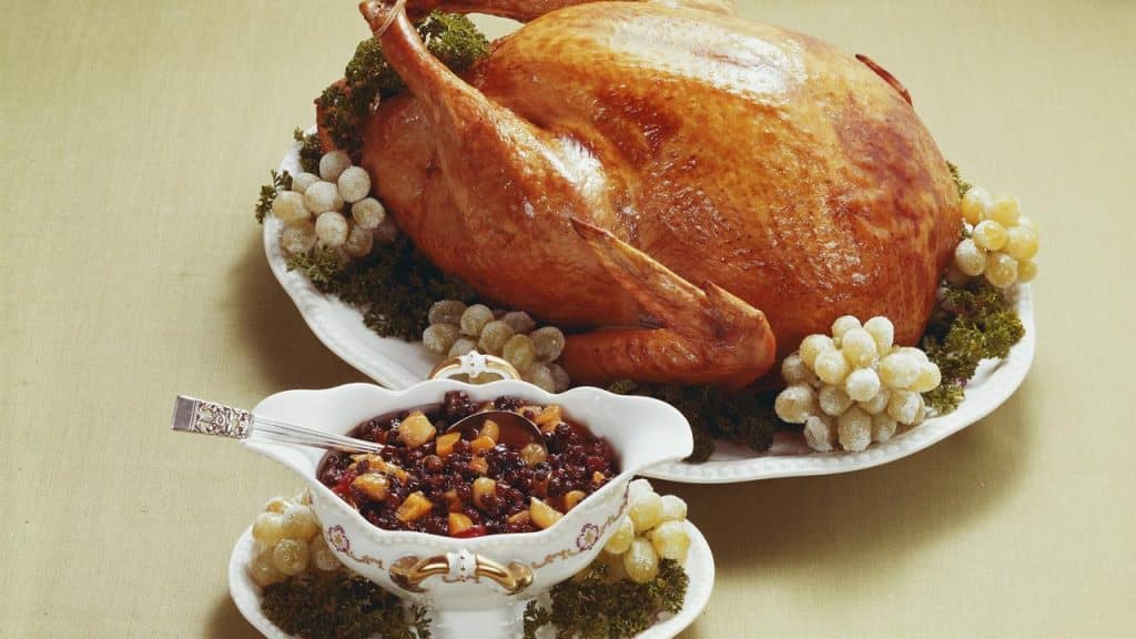 A roasted turkey on a platter with a bowl of cranberry sauce.