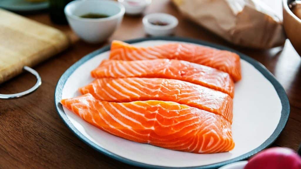 A plate of raw salmon fillets with prep bowls in the background.