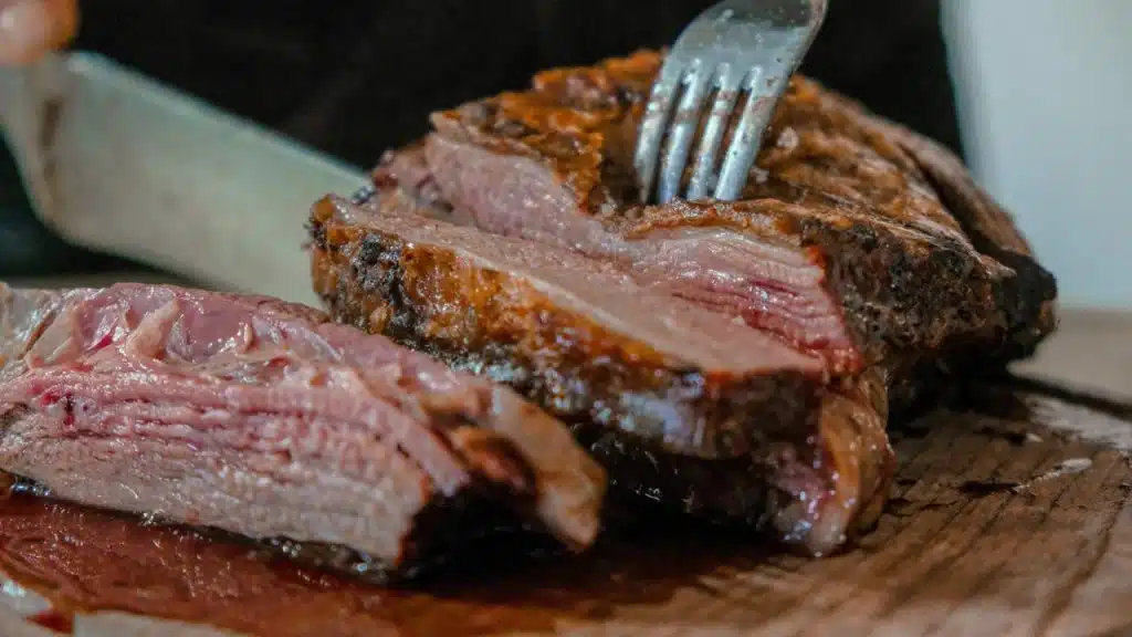 A sliced medium-rare steak on a cutting board being pierced with a fork.